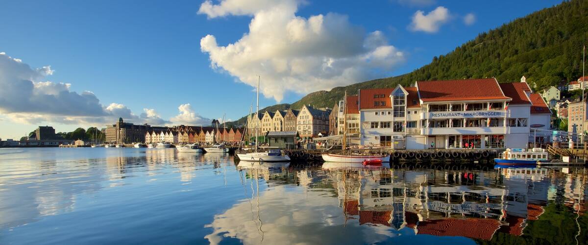 A calm harbor with boats, traditional buildings, and a mountain backdrop.