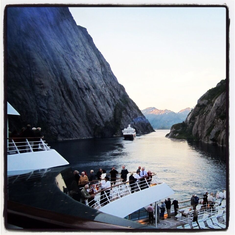 A cruise ship navigating through a narrow fjord flanked by steep cliffs.