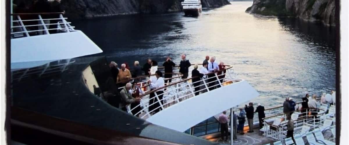 A cruise ship navigating through a narrow fjord flanked by steep cliffs.