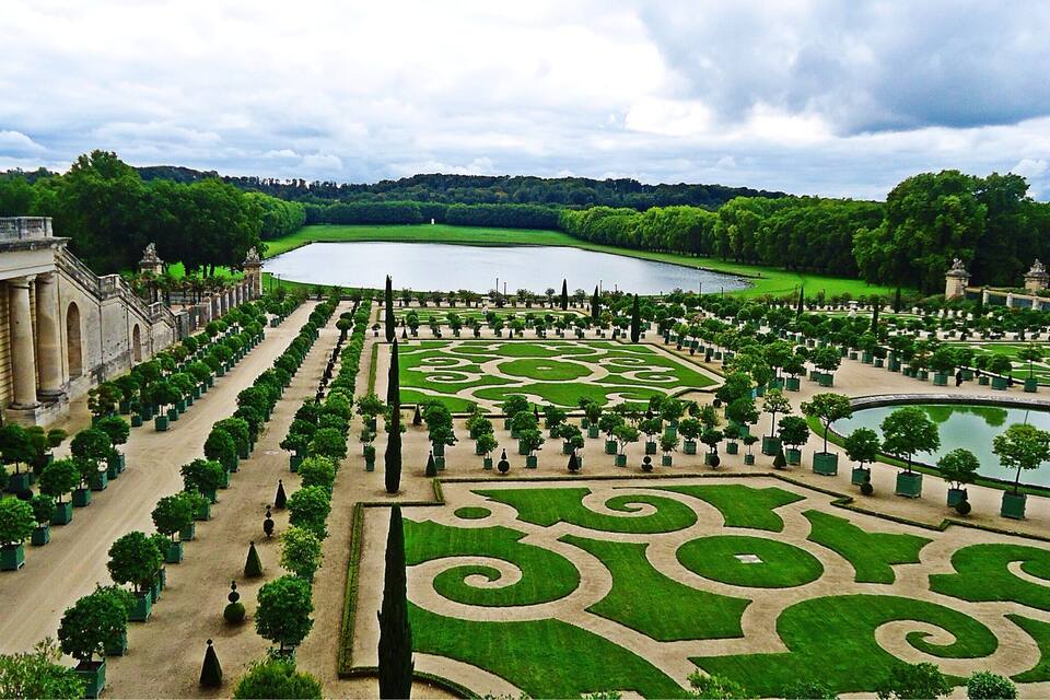 Ein formal angelegter Garten mit geometrischen Mustern, einem großen Teich und klassischer Architektur.