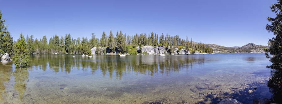 A clear lake surrounded by dense forest and rocky outcrops.