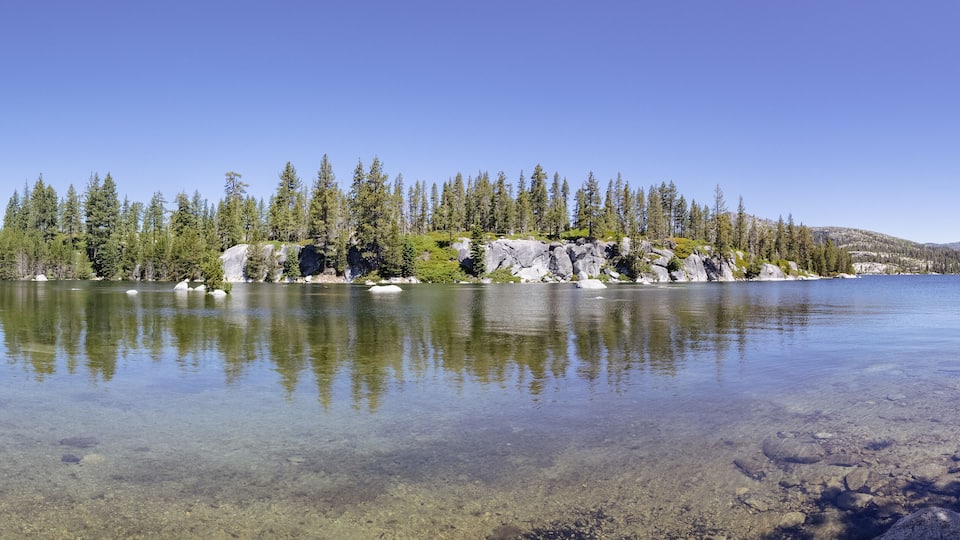 A clear lake surrounded by dense forest and rocky outcrops.