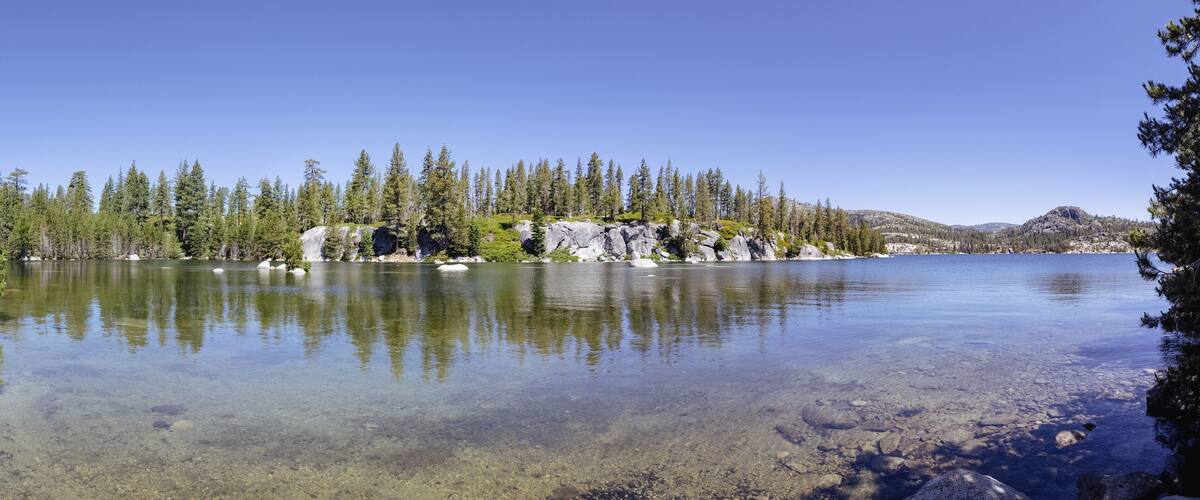 A clear lake surrounded by dense forest and rocky outcrops.