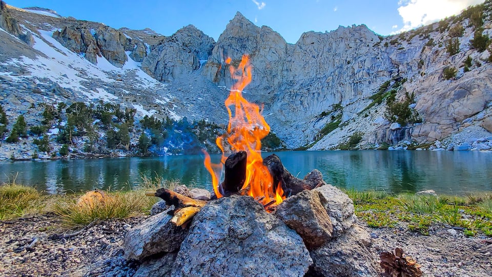 A campfire surrounded by a rocky landscape with a lake and mountains in the background.