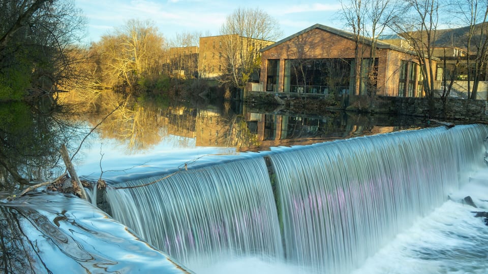 A waterfall, a stone bridge, and buildings in the background.