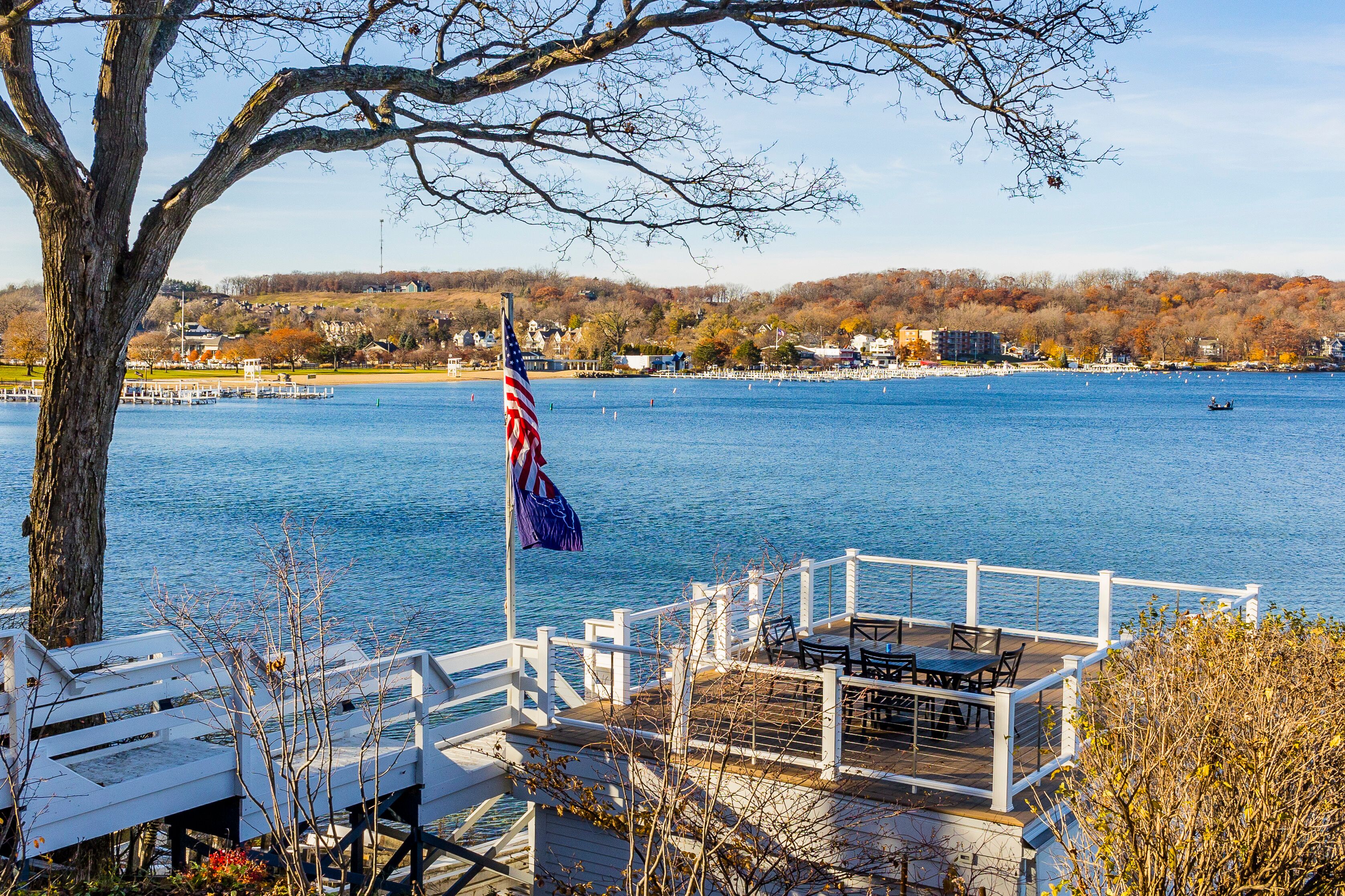 A waterfront with a dock, an American flag, and a view of a lake with boats.