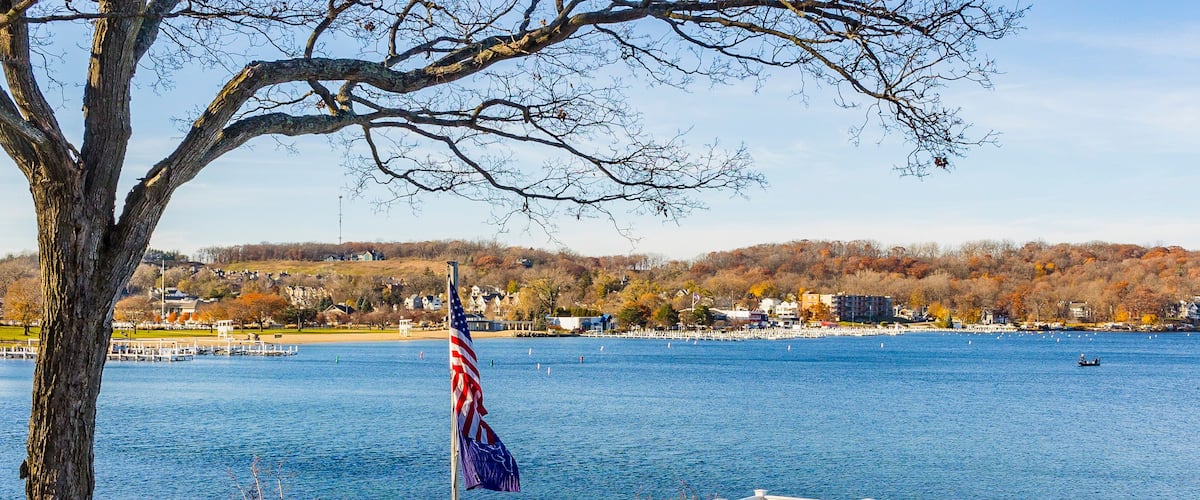 A waterfront with a dock, an American flag, and a view of a lake with boats.