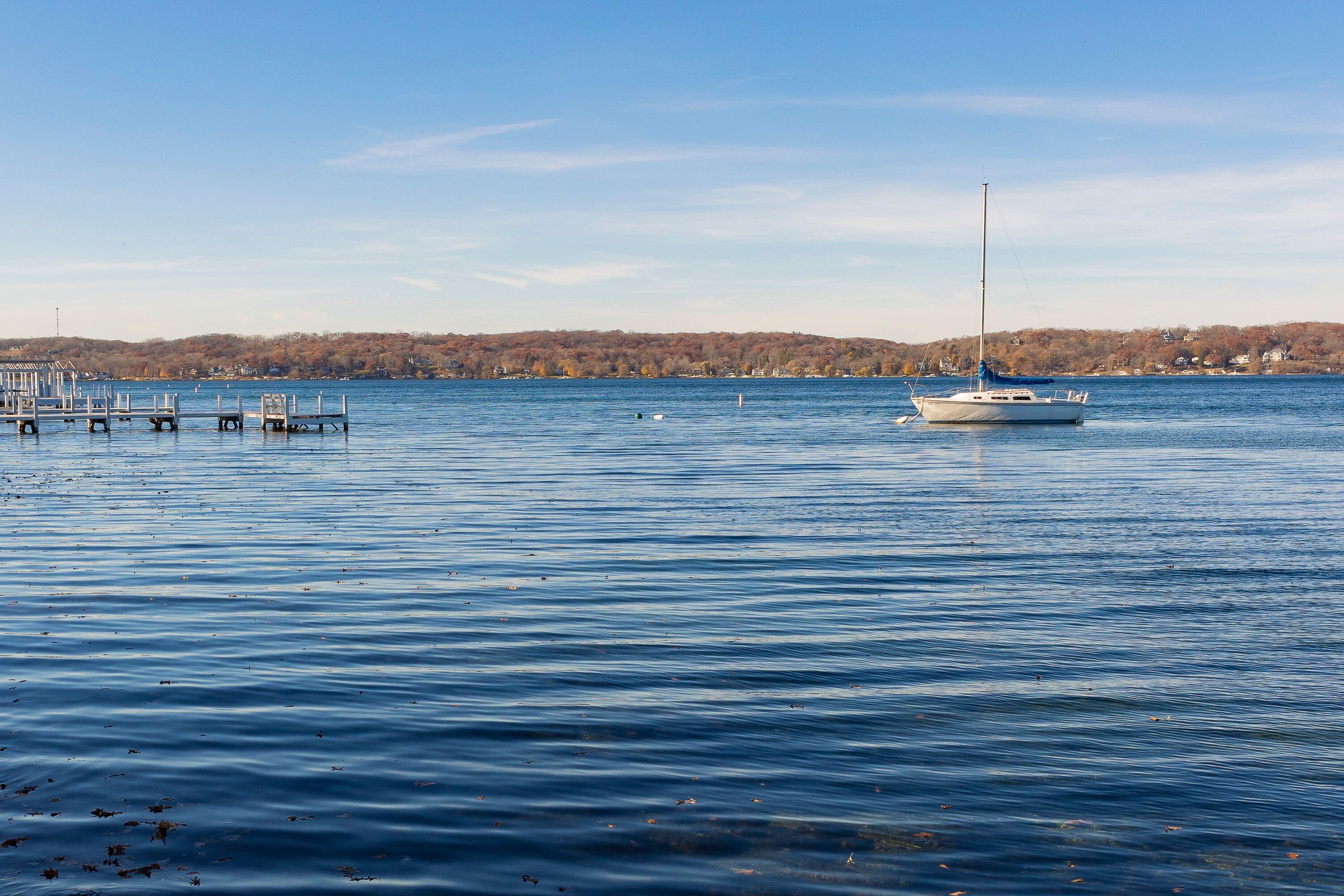 A single sailboat anchored in a lake near a pier on a clear day.