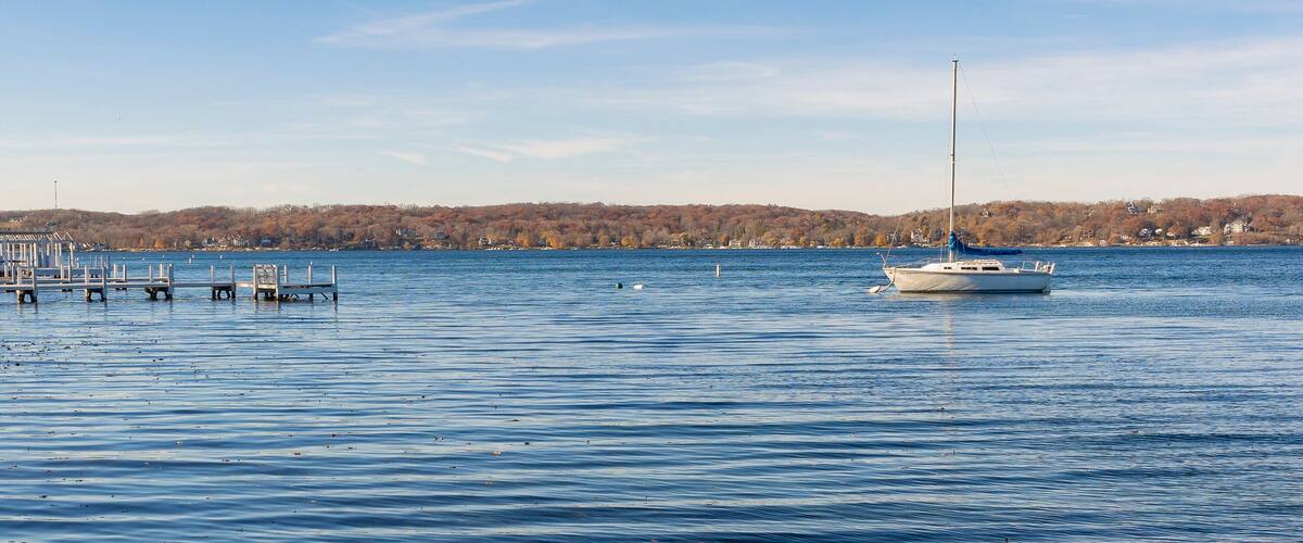 A single sailboat anchored in a lake near a pier on a clear day.