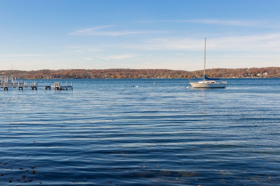 A single sailboat anchored in a lake near a pier on a clear day.