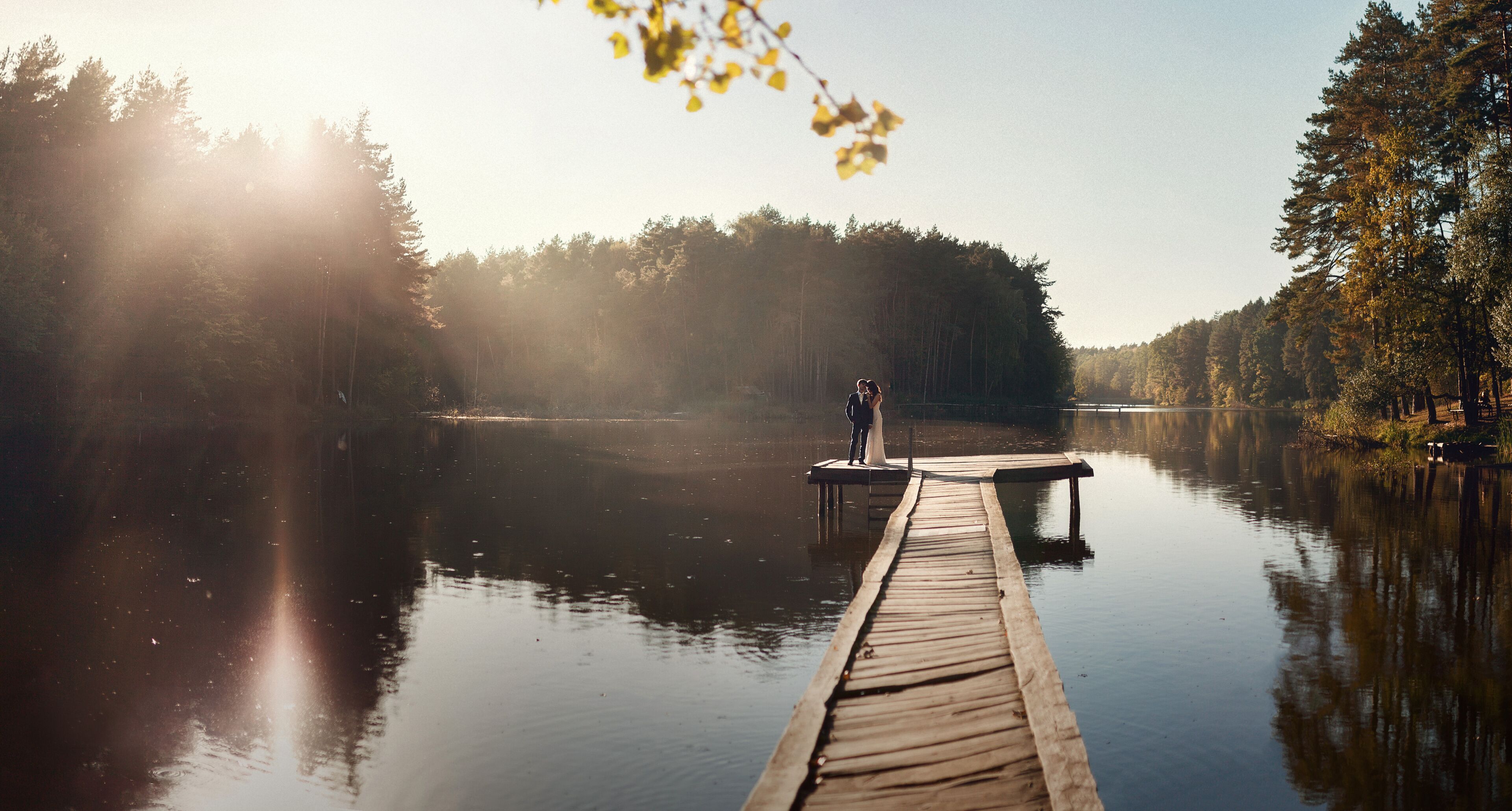 A wooden dock extending into a calm lake surrounded by dense forest.