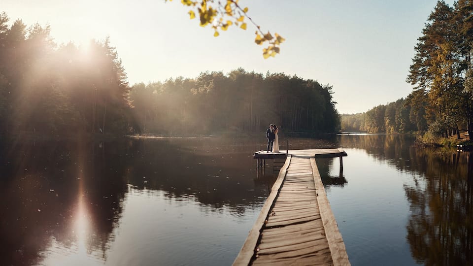 A wooden dock extending into a calm lake surrounded by dense forest.