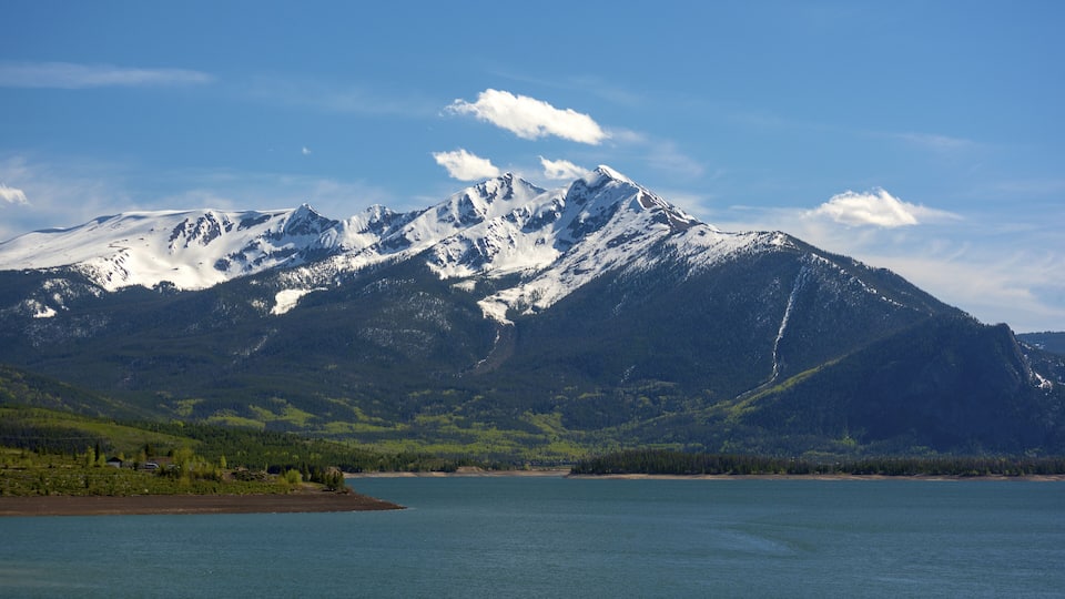 A snow-capped mountain range with a lake in the foreground.