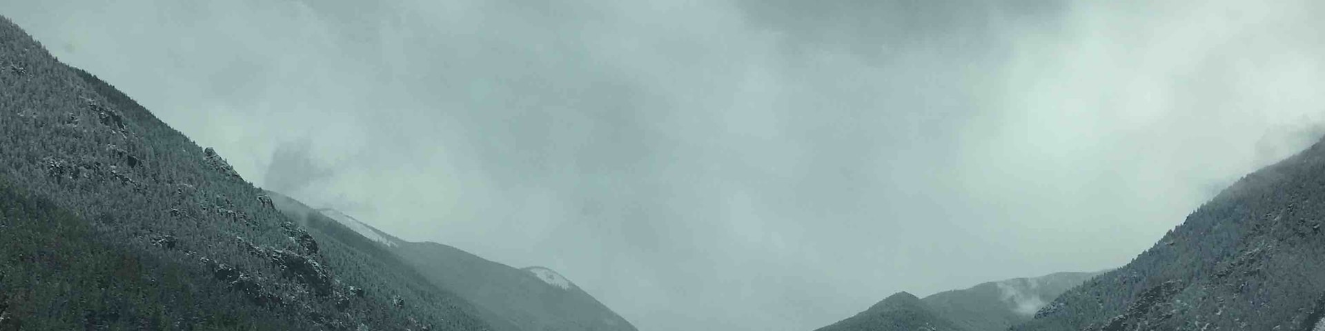 A highway curving through a mountainous landscape with a lake and a cloudy sky.