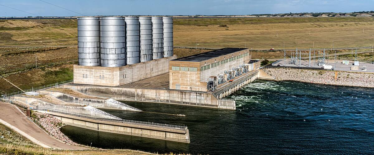 Uma centrais hidroelétrica com vários tanques de armazenamento grandes e uma barragem sobre um rio.