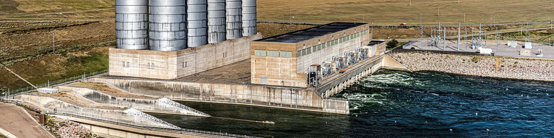 A hydroelectric power plant with multiple large storage tanks and a dam across a river.