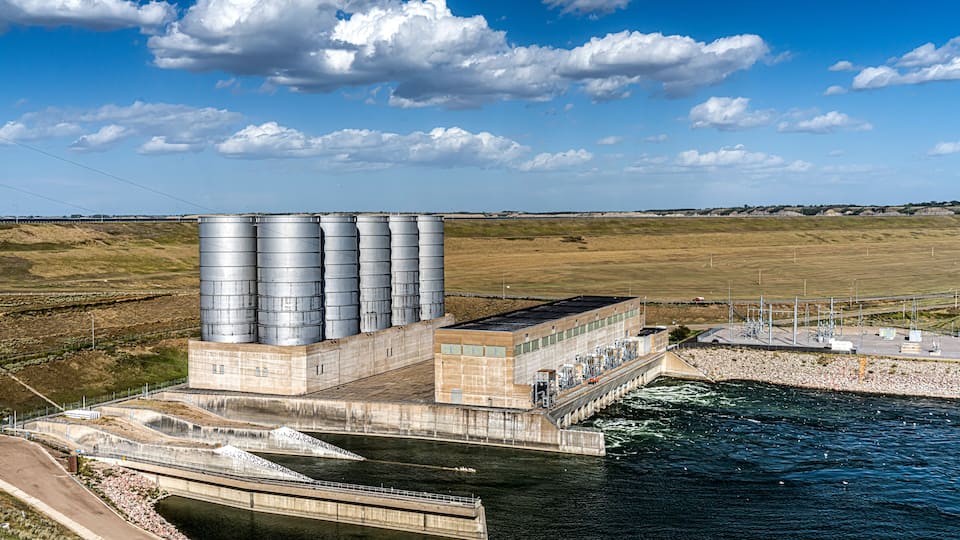 A hydroelectric power plant with multiple large storage tanks and a dam across a river.