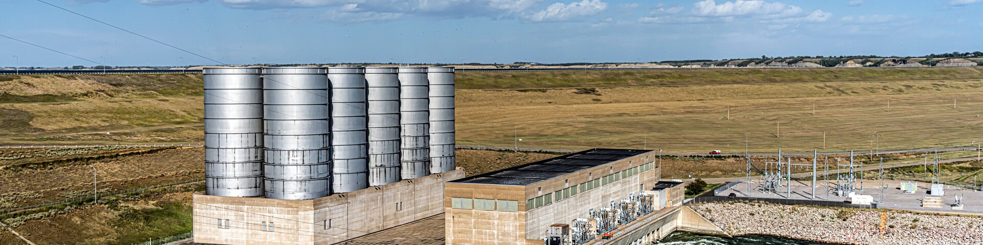 Una central hidroeléctrica con múltiples tanques de almacenamiento grandes y una presa sobre un río.
