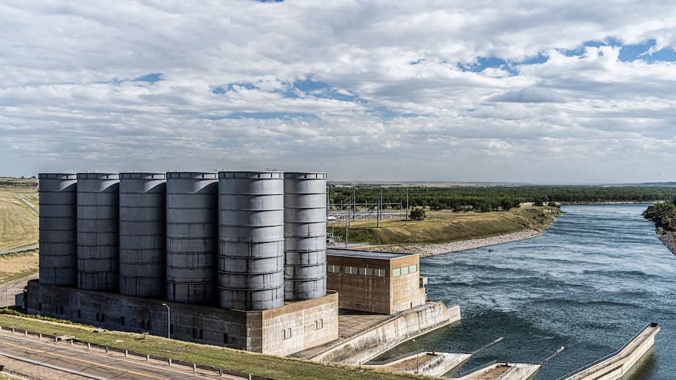 A large industrial facility with multiple silos by a river.