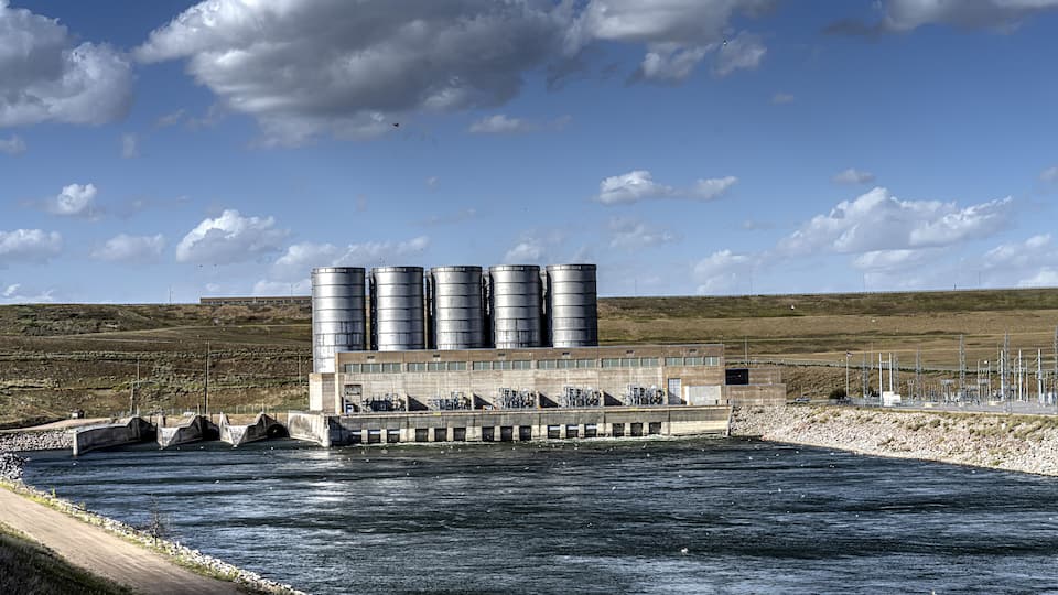 A hydroelectric power plant with multiple water turbines and storage silos by a river.