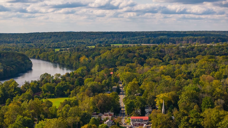 A river winding through a densely wooded area with a small town and a church.