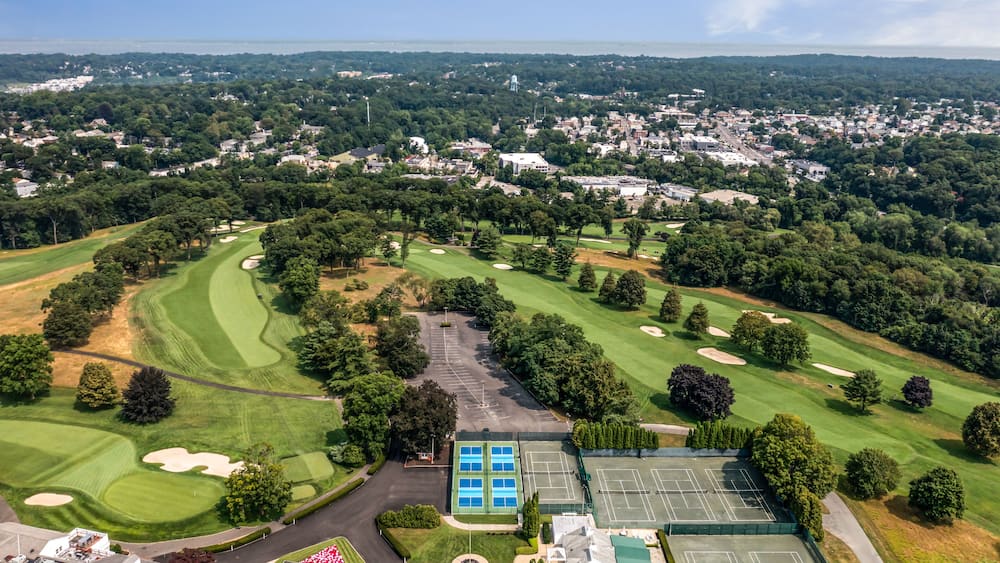 An aerial view of a golf course with a tennis court and a parking lot.