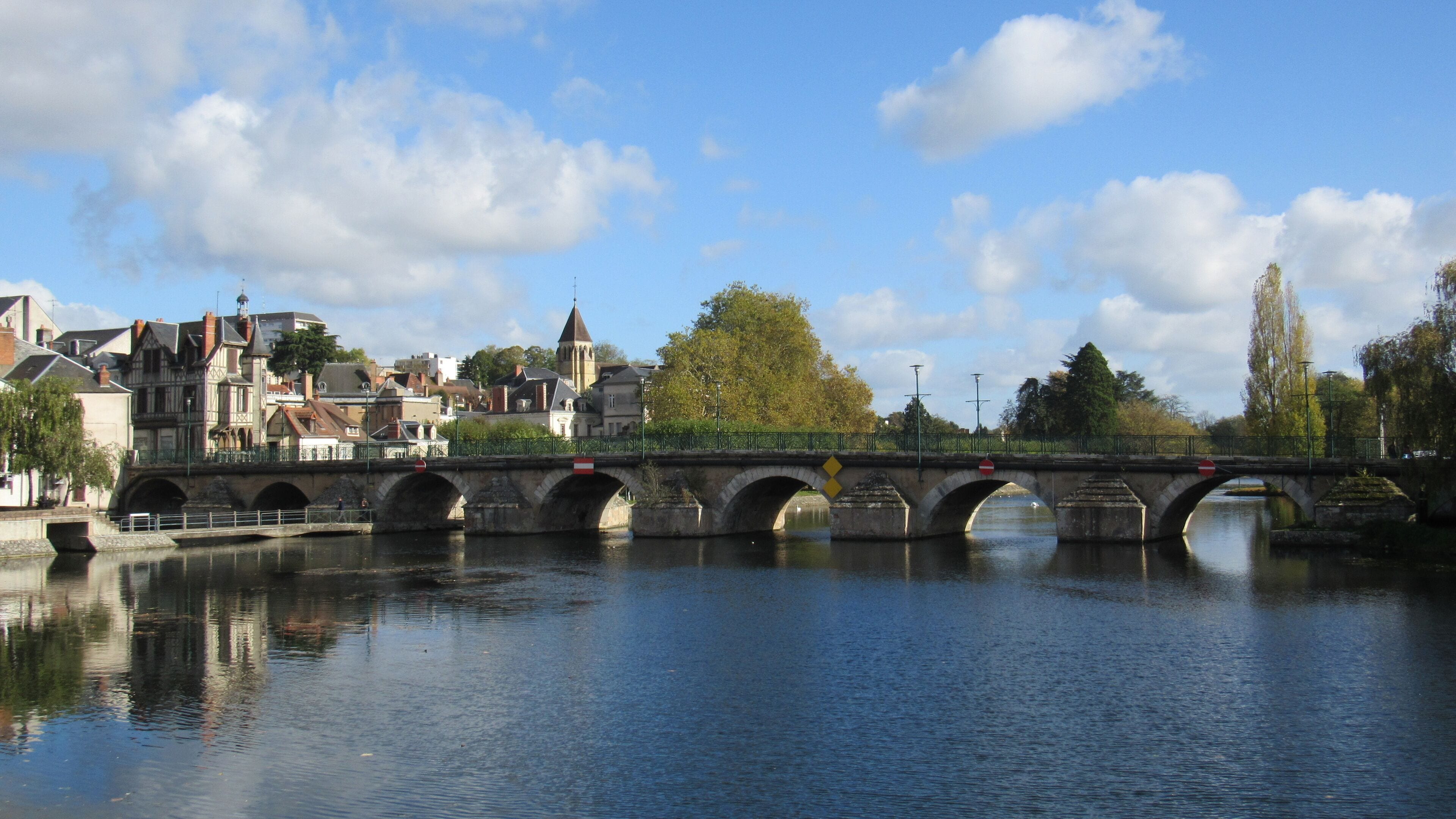A stone bridge over a calm river, surrounded by historic buildings and trees.
