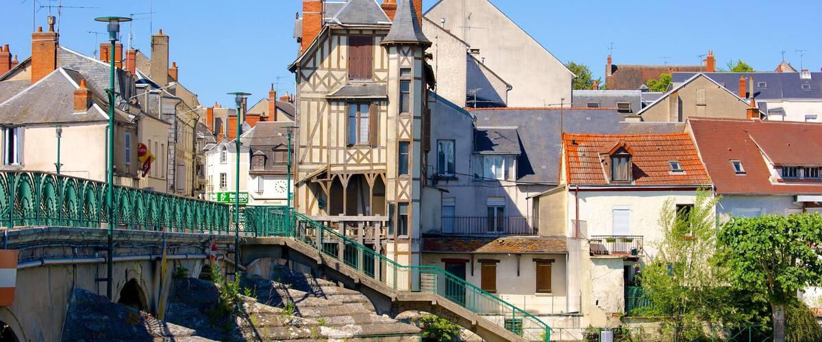 A stone bridge with a green railing, a river, and historic buildings with varied architecture.
