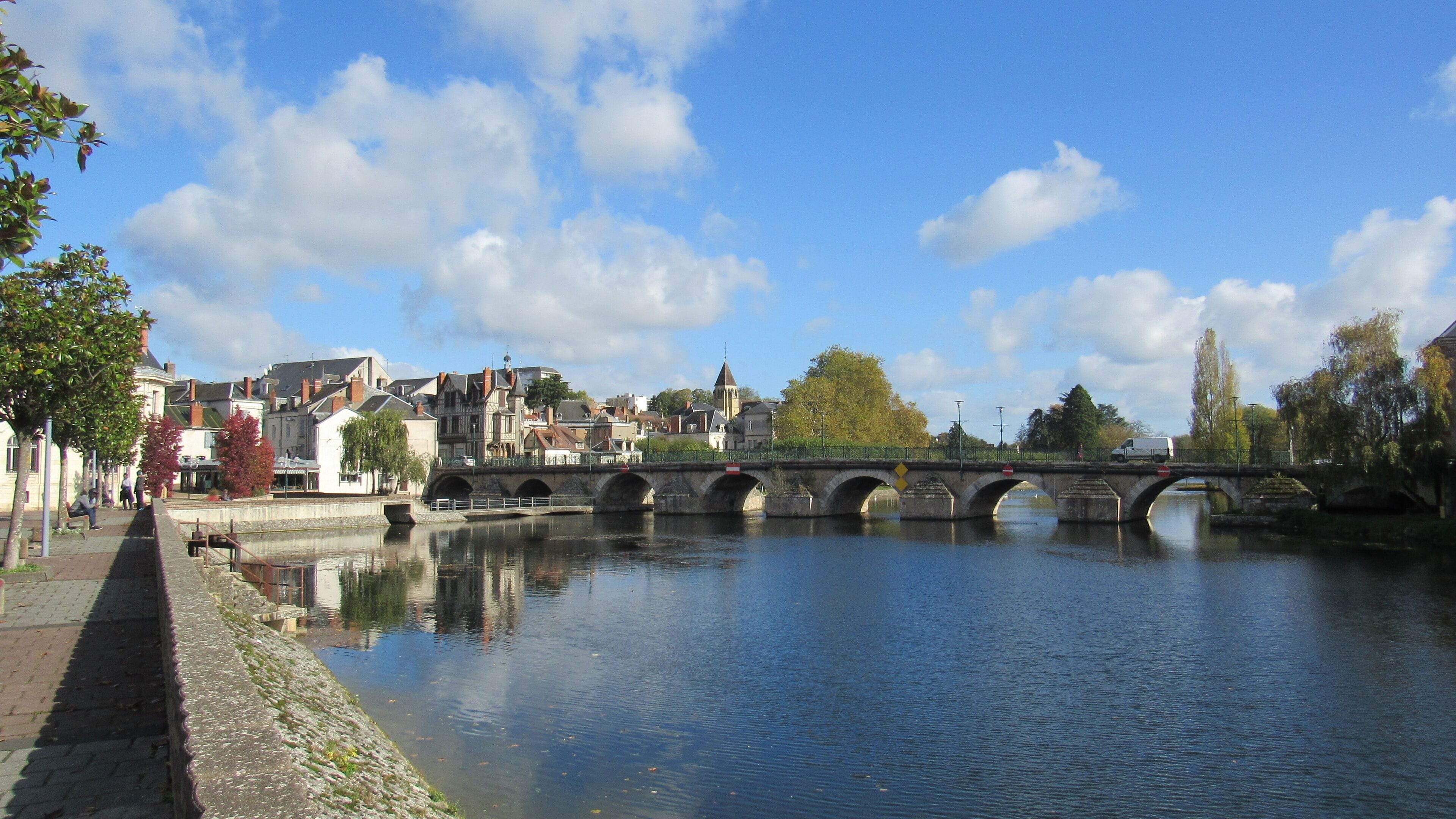 A stone bridge over a calm river, surrounded by historic buildings and trees.