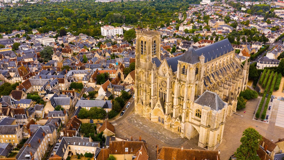 A cathedral with a tall tower, surrounded by a densely packed town with historic buildings.