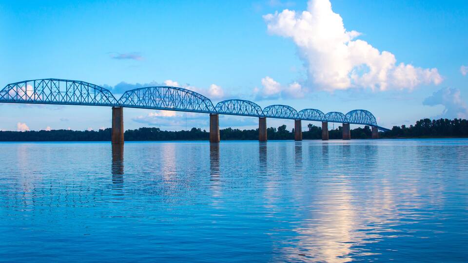 A steel bridge over a calm body of water with a clear sky.