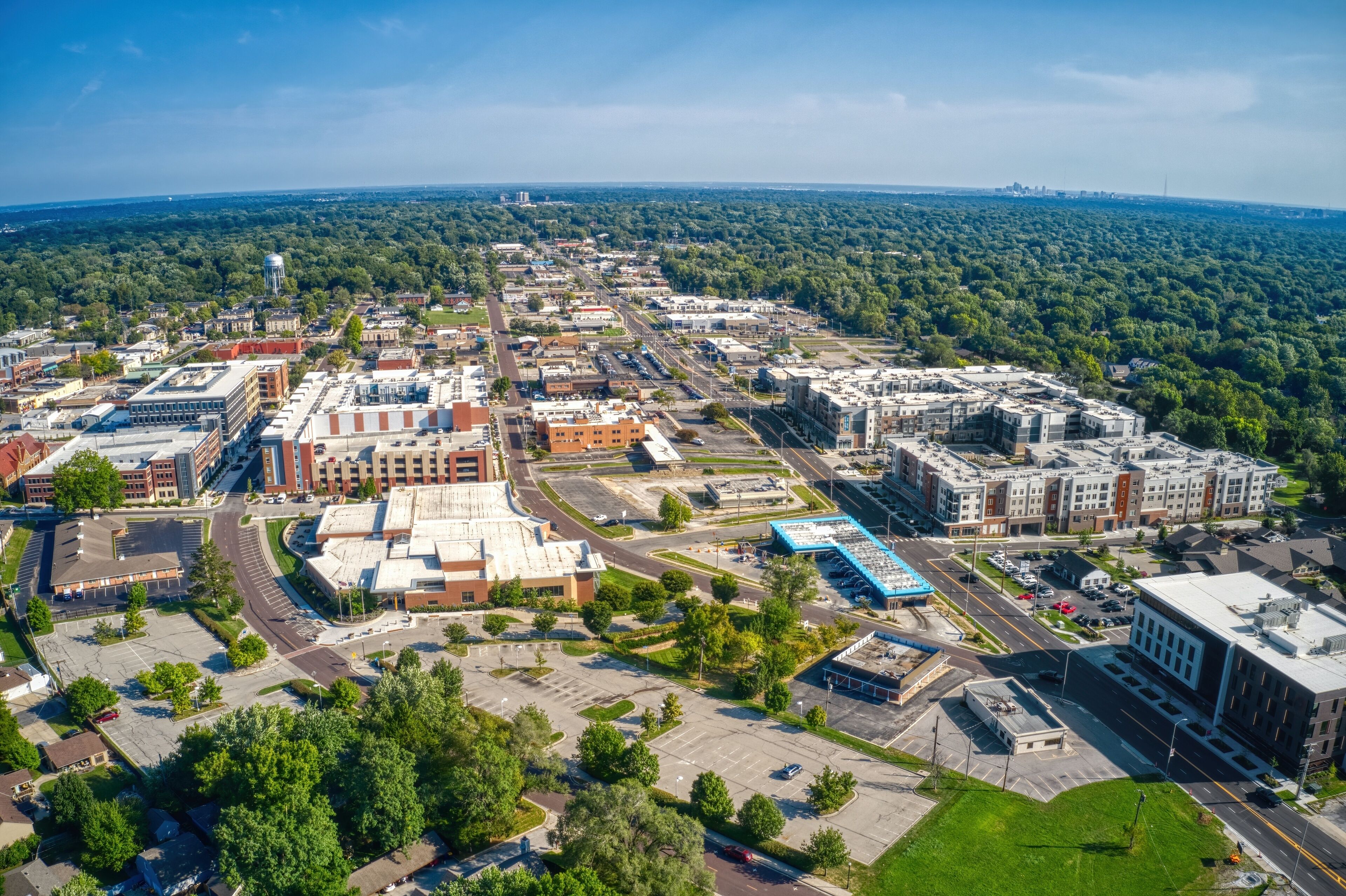 An aerial view of a city with a mix of commercial buildings, parking lots, and green spaces.