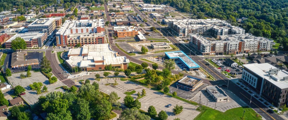An aerial view of a city with a mix of commercial buildings, parking lots, and green spaces.