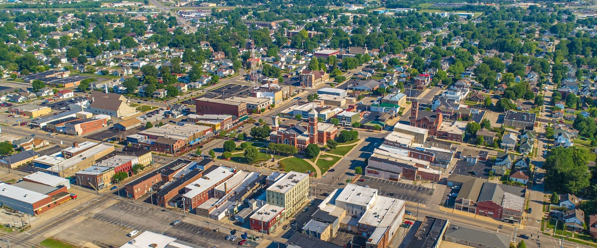 An aerial view of a small town with a mix of residential and commercial buildings, a railroad track, and a large open area in the center.