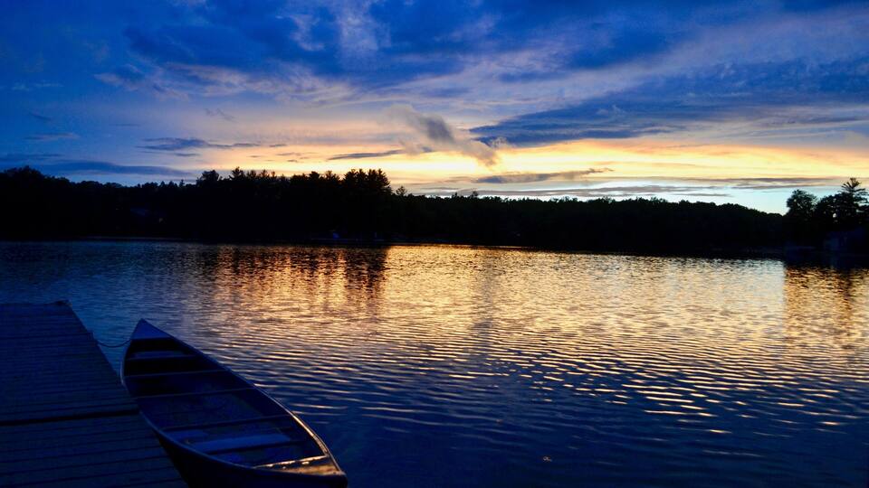 A wooden dock extending into calm water at dusk with a sunset in the background.
