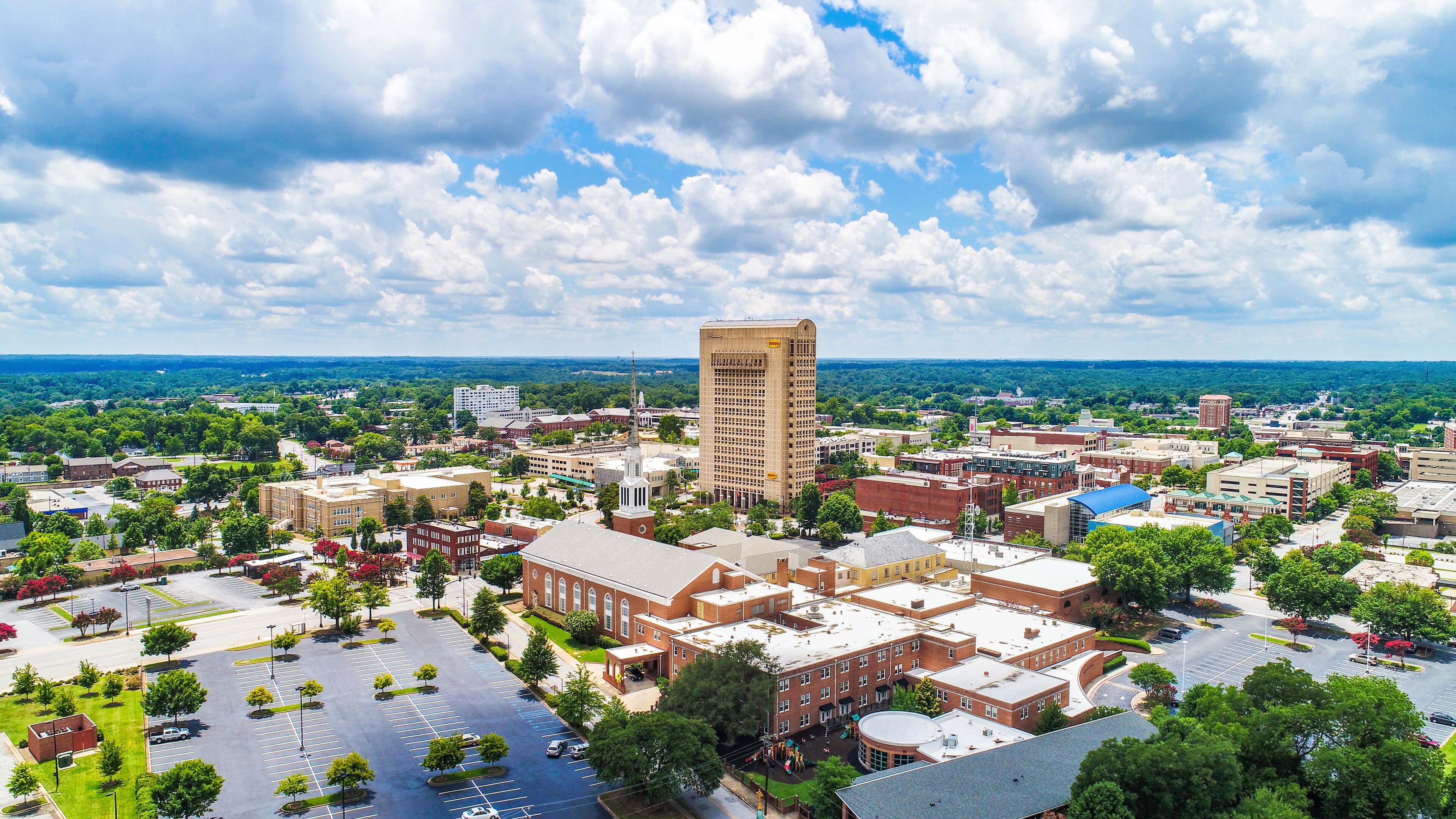 A cityscape with a prominent tall building, a mix of commercial and residential buildings, and a large parking area.
