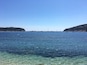 Mar tranquila con barcos y boyas, agua cristalina y colinas al fondo.