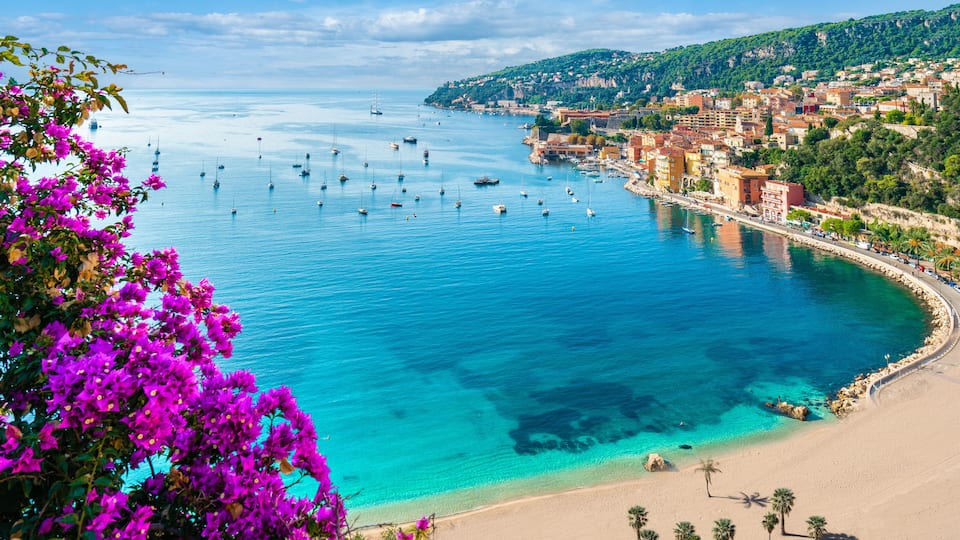 A coastal town with a clear blue sea, boats, and a sandy beach.