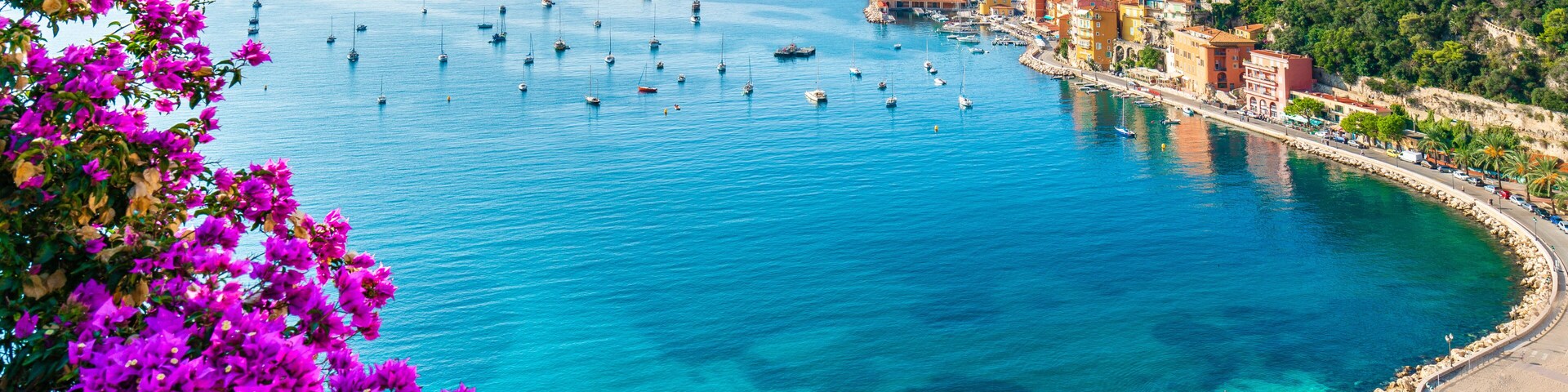 Uma vila costeira com mar azul cristalino, barcos e uma praia de areia.