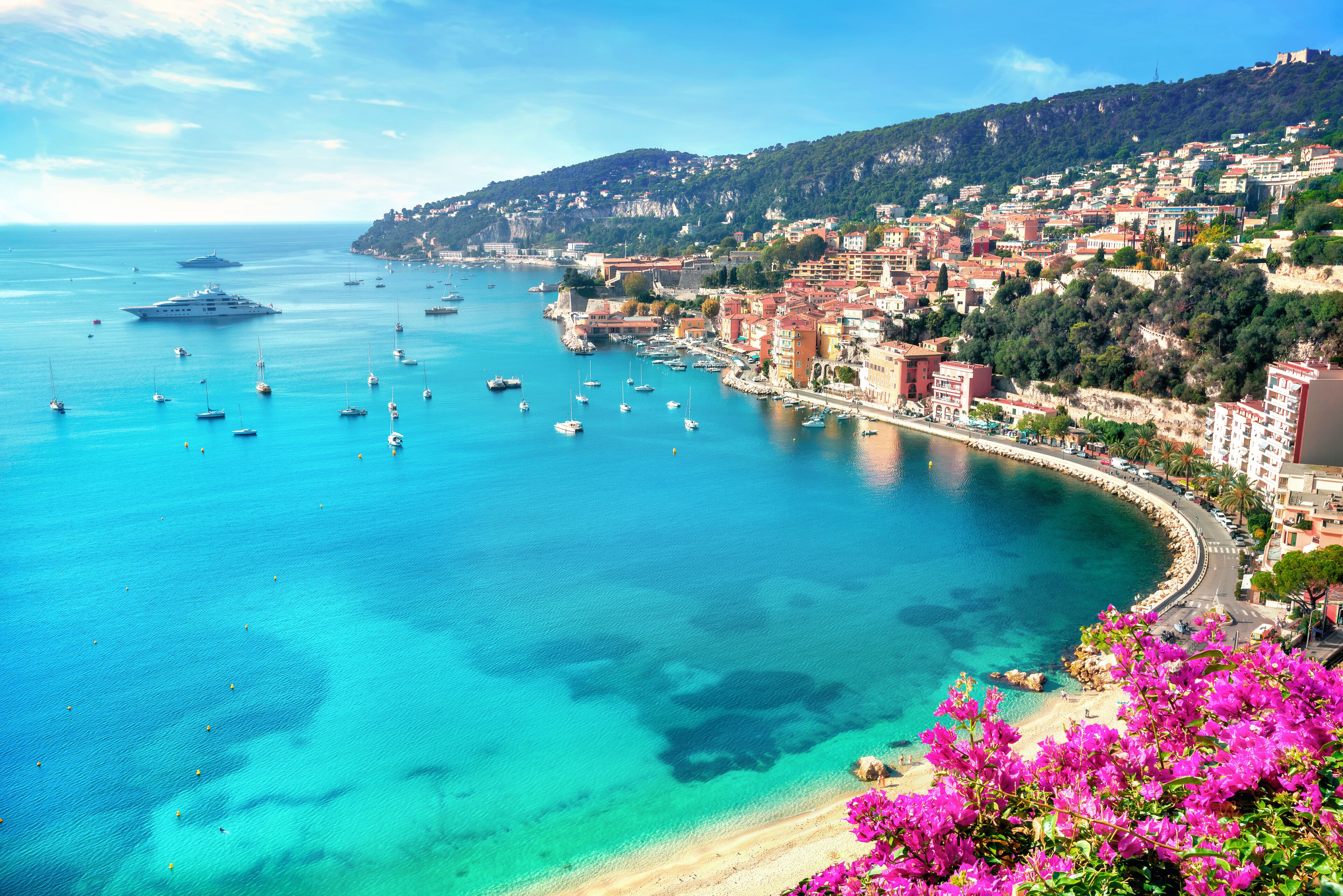 A coastal town with a bay, boats, and a hill with buildings.