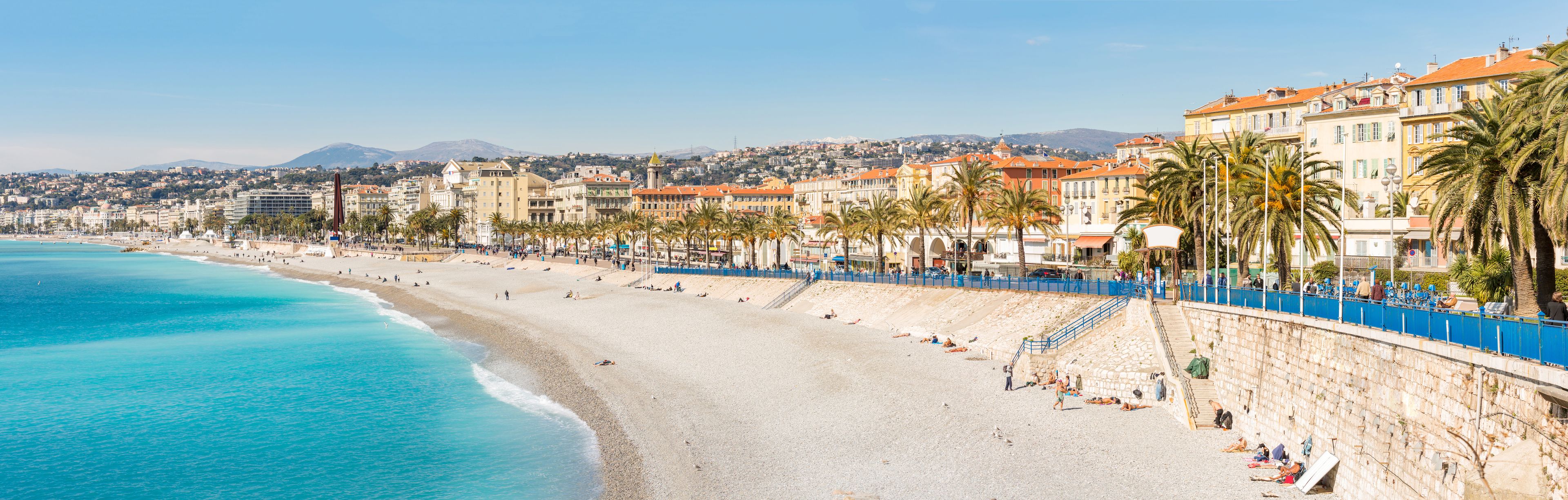 Un paysage urbain côtier avec une vaste plage de sable, des palmiers et des bâtiments historiques.