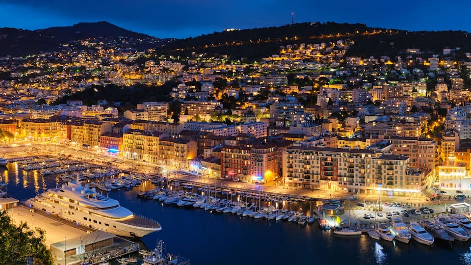A nighttime cityscape with a marina filled with yachts.