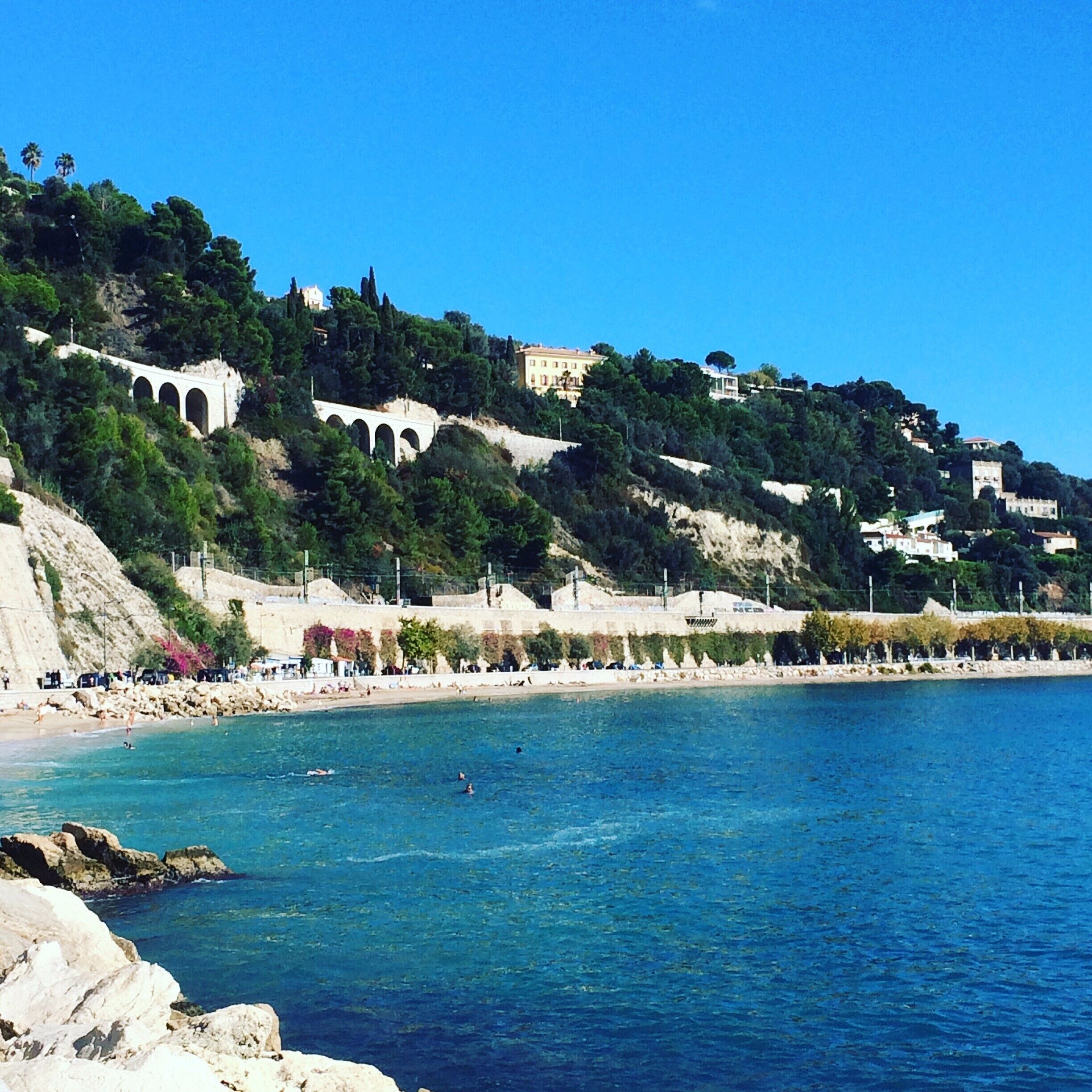 Un pueblo costero con playa, mar azul cristalino y edificios en una colina.