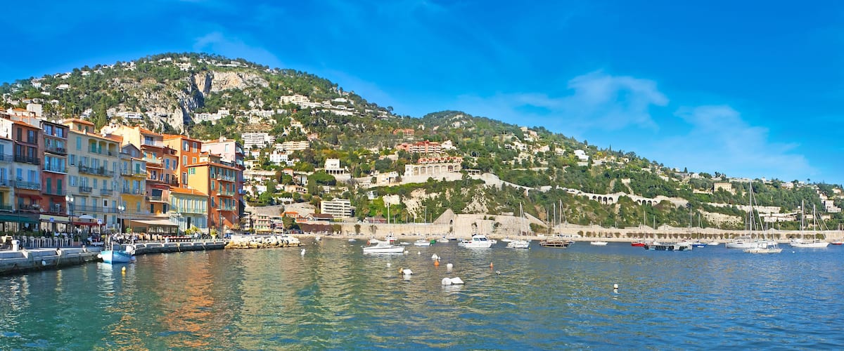 A coastal town with colorful buildings, a harbor with boats, and a hill with a castle-like structure.