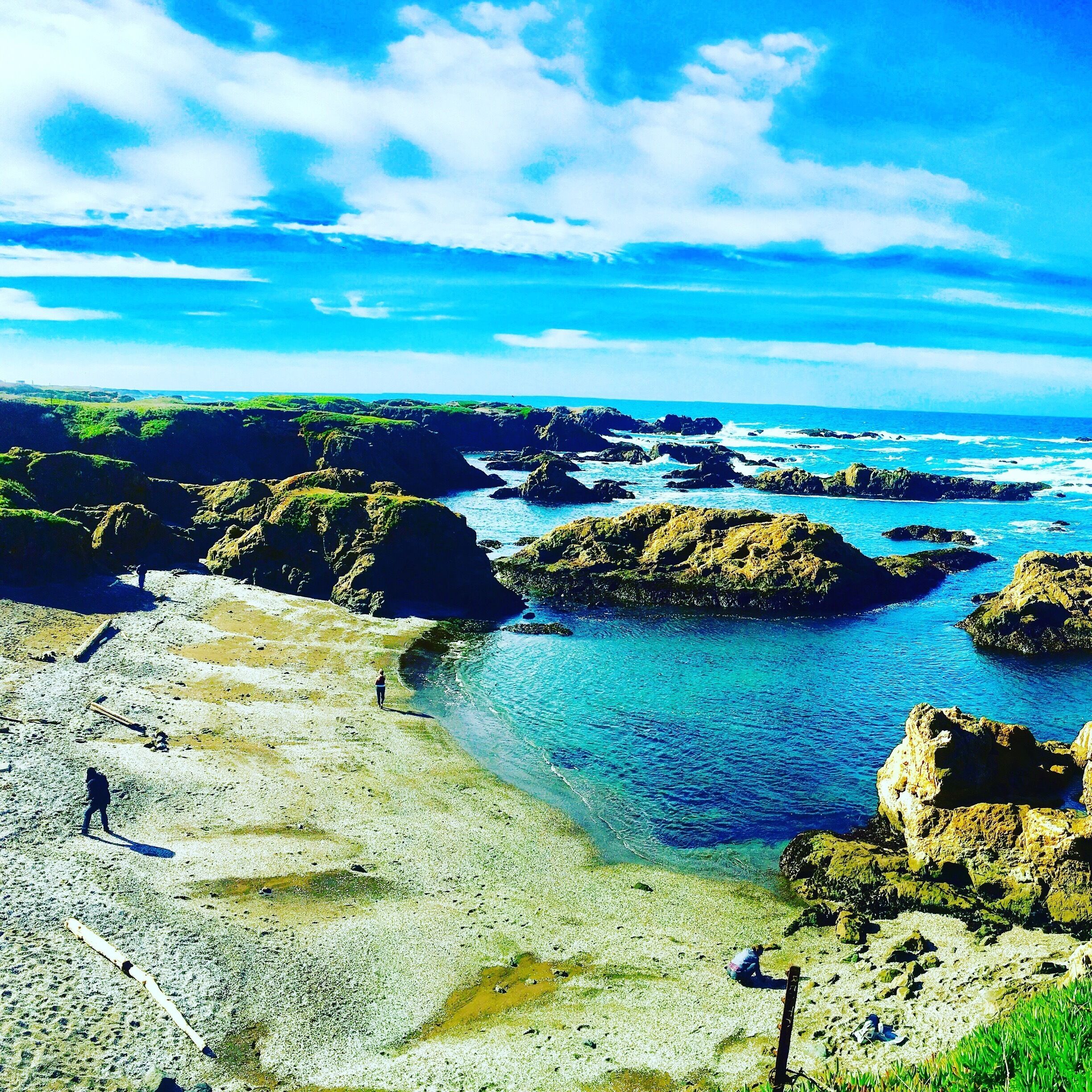 A rocky coastline with clear blue waters and a person walking on the beach.
