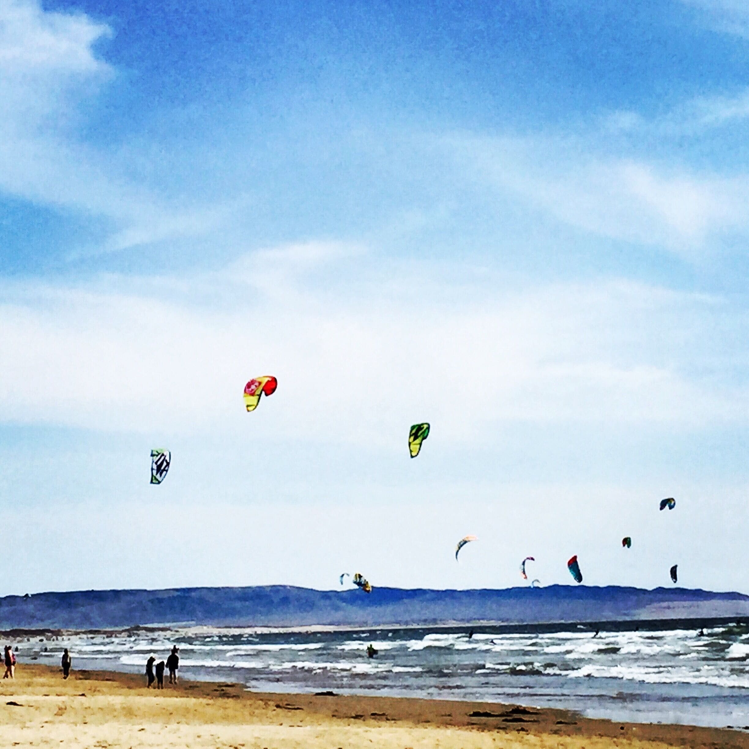 A beach with people and multiple kites flying in the sky.
