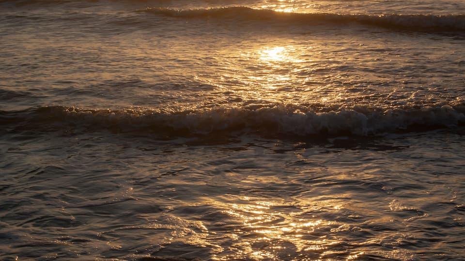A sunset over the ocean with waves reflecting the sunlight.