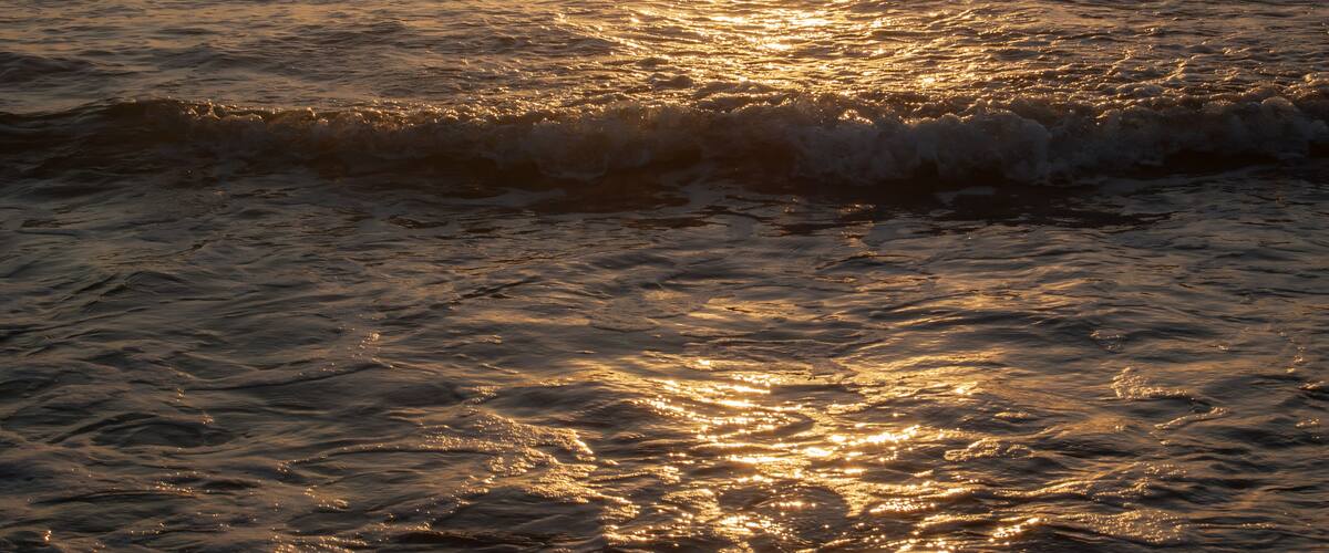 A sunset over the ocean with waves reflecting the sunlight.