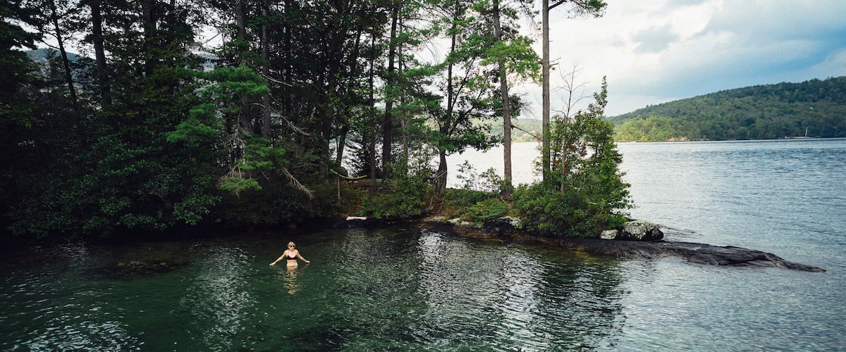 A person swimming in a lake surrounded by dense forest and hills.