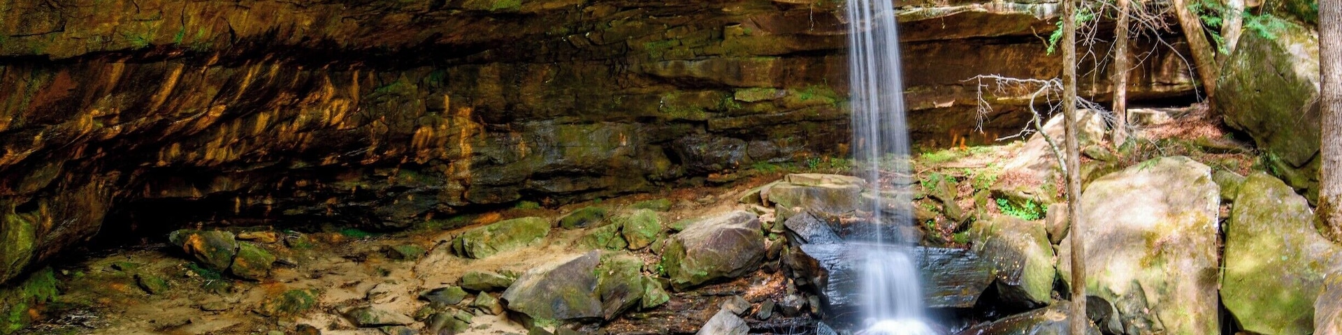Uma cascata descendo sobre pedras em uma área arborizada.